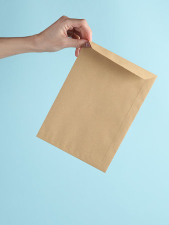 Kraft postal envelope in a female hand on a blue backgroundの写真素材