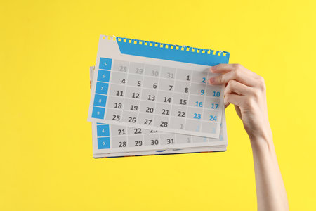 Hand holds sheets of the calendar on yellow background. Planning, travel, business conceptの写真素材