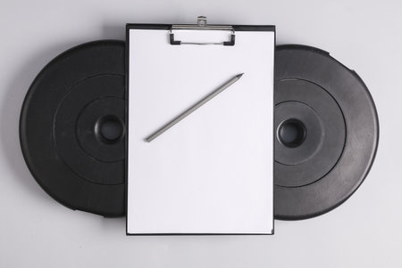 training program. Clipboard with blank white sheet and barbell discs on gray background