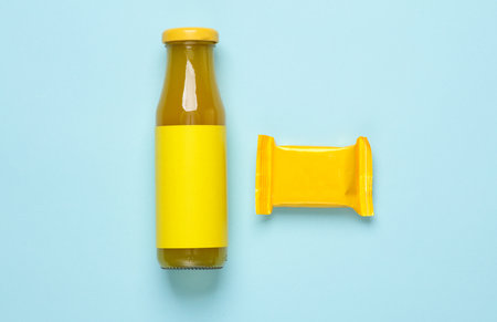 Glass bottle of juice and yellow candy packaging on a blue background. Layout, Template for designの写真素材