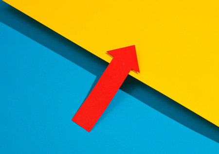 Red pointing arrow on a yellow-blue backgroundの写真素材