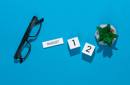 White cube calendar with date august 12 with eyeglasses and plant on blue background. Deadline, planning, business conceptの写真素材