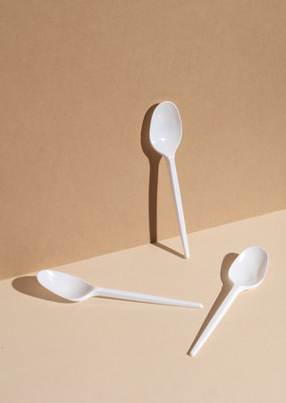 White plastic spoons on a beige background with a shadow. creative layout