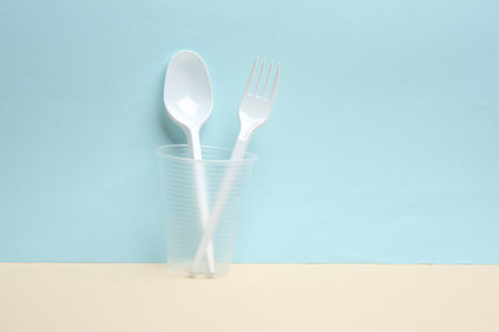Plastic fork and spoon in glass on a blue-yellow background. creative layoutの写真素材