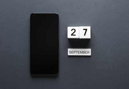 White wooden block calendar with date september 27 and smartphone on gray background. business, deadline, planningの写真素材