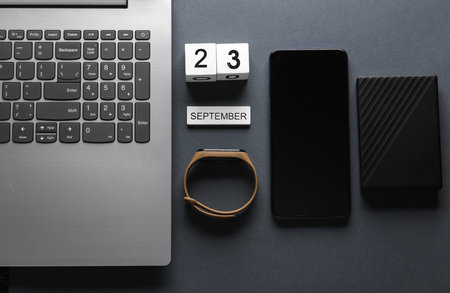 White wooden block calendar with date september 23 and modern gadgets on gray background. top view