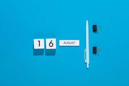 White cube calendar with date august 16 with binder clips and pen on blue background. Deadline,...