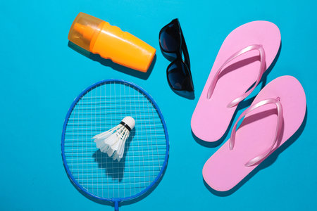 beach holidays. Badbinton racket, shuttlecock, flip flops, sunblock and sunglasses on a blue...
