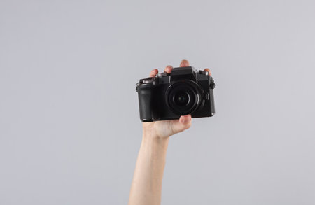 Woman's hand holding a modern digital camera on gray background