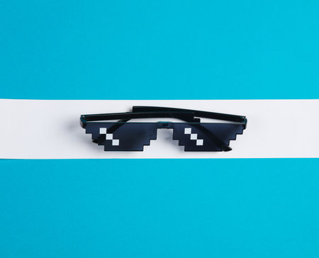 Pixel sunglasses on a blue background with a white stripe. Creative layout, minimalism, weight lossの写真素材