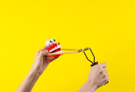 Hands holding slingshot with joke jaw on a yellow background.の写真素材