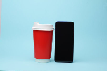 Disposable coffee cup with smartphone on blue backgroundの写真素材