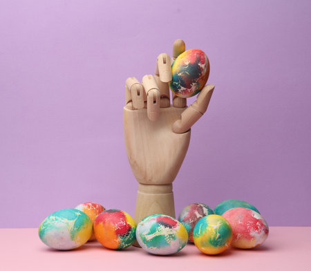 Wooden hand holds a colored Easter egg on a pastel background. Minimal easter still lifeの写真素材