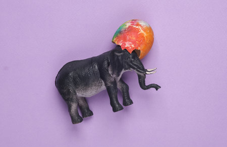 Conceptual Easter still life. Toy elephant with a colored easter egg on a purple background