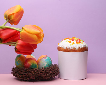Easter cake with colored eggs in nest and tulips on pastel color background. Easter still life