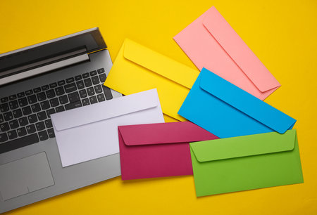 Laptop and Set of colored envelopes on yellow background. Creative layout