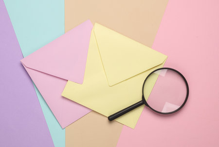 Two pastel colored envelopes with a magnifying glass on a pastel colored backgroundの写真素材