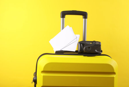 Yellow suitcase, travel bag or luggage with retro camera and blank photo mockups on yellow background. Summer vacation, travel, trip concept.の写真素材