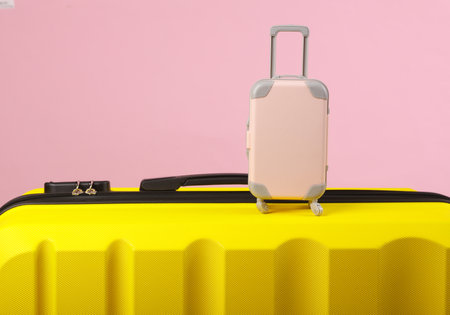 Yellow plastic travel suitcase and miniature on pink background. Luggage, tourism, vacation, relocation conceptの写真素材