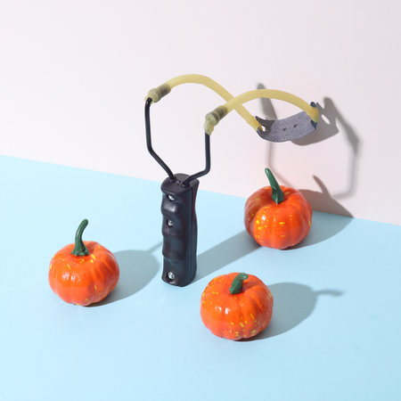 Conceptual halloween still life. Slingshot with pumpkins on a pastel backgroundの写真素材