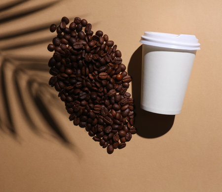 Coffee bean and white paper cup on brown background with palm leaf shadow. creative summer layoutの写真素材