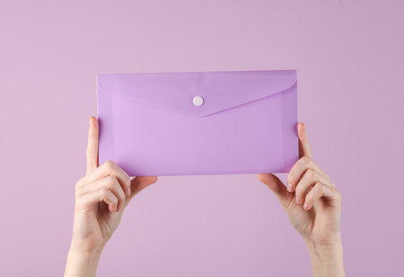 Female hands holding purple plastic envelope folder on a purple background. Business conceptの写真素材