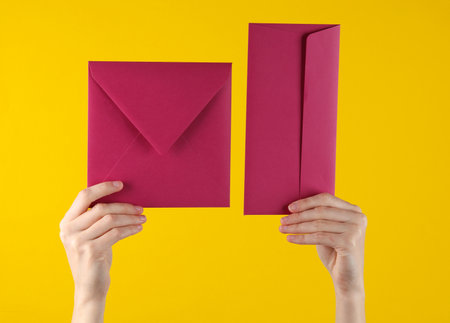 Female hands holding two pink envelopes on yellow background