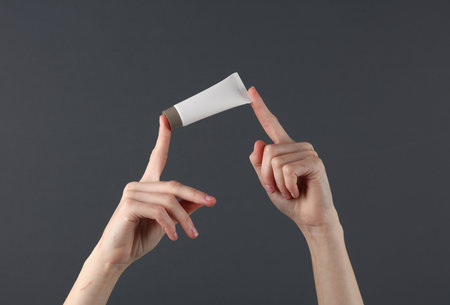 Women's hands hold a white cream tube on a dark background. Beauty mockupの写真素材