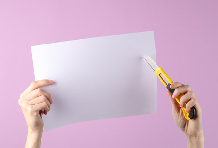 Stationery knife iand a4 paper sheet n hands on purple backgroundの写真素材