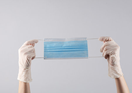 Doctor's female hands in medical gloves hold a medical mask on gray background. Medicine concept
