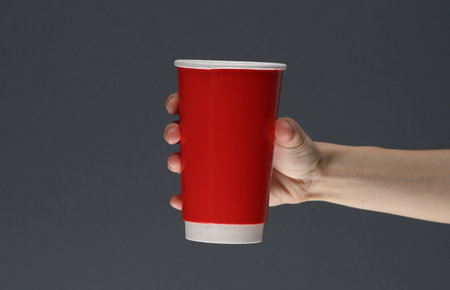 Female hand holding red disposable cup for hot drinks on a dark background