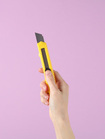 Stationery knife in hand on purple backgroundの写真素材
