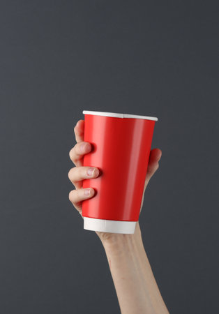 Female hand holding red disposable cup for hot drinks on a dark background