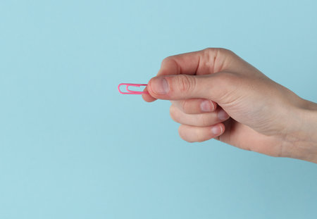Woman's hand holding a pink paper clip on blue backgroundの写真素材