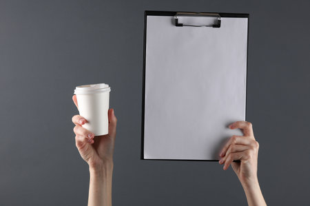 Female hands holding white binder folder and coffee cup on dark background. Business conceptの写真素材
