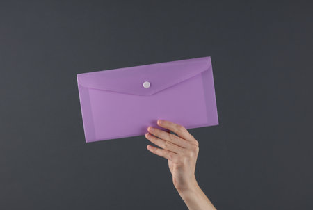 Female hand holding purple plastic envelope folder on a dark background. Business conceptの写真素材