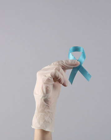 A hand in a medical glove holds a blue male prostatitis awareness ribbonの写真素材