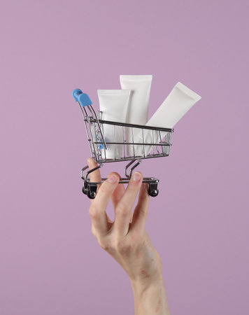 Mini supermarket trolley with white cream tubes on palm of hand, purple backgroundの写真素材