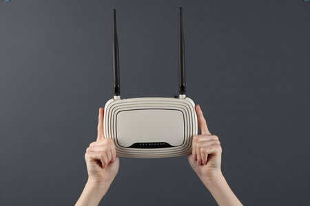 Hands holding a wi-fi router on dark gray background