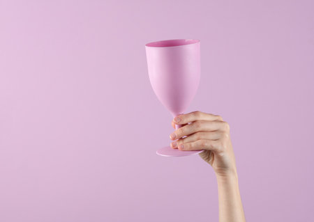 Hand holding a plastic glass goblet on a lavender color pastel backgroundの写真素材
