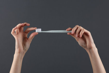 Hands holding toothbrush on a dark gray background. Caring for teeth, oral hygiene conceptの写真素材