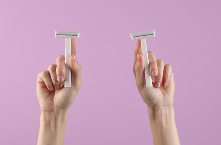 Women's hands holding razor on a pastel background. Depilationの写真素材
