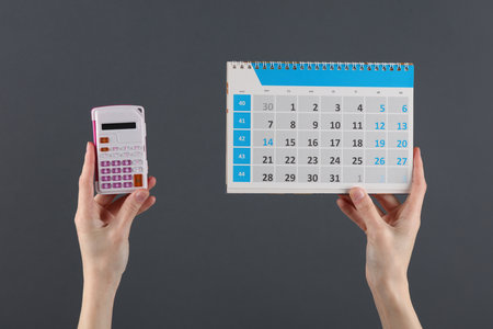 Hands holding a calculator and a calendar on a dark background. Business concept, deadlineの写真素材