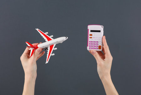 Hands holding a calculator and toy air plane on a dark background. Travel coastの写真素材
