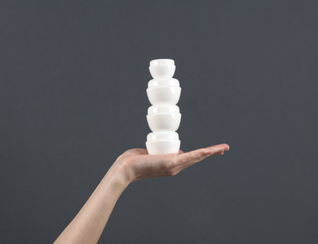 Stack of white jars of cream on the palm of hand, gray background. Mockup, template for designの写真素材