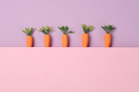 Plastic miniature carrots on a pastel background. Minimal, conceptual food still life, creative layoutの写真素材