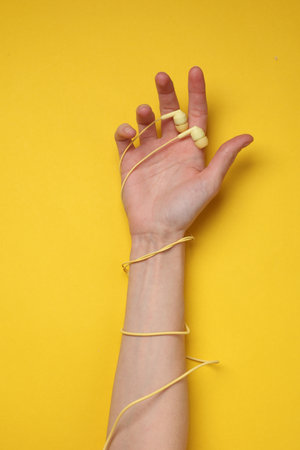 Hand wrapped with wired headphones on a yellow background. Music loverの写真素材