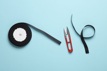 Roll of black satin ribbon for decoration and scissors on blue pastel backgroundの写真素材