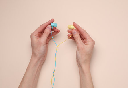 Female hands hold blue and yellow wired headphones on a beige background