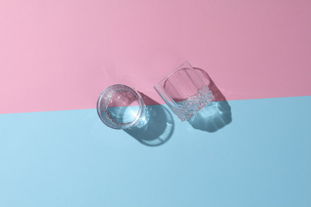 Glasses of water with reflection and shadow on pink blue pastel background. Minimalism. Top viewの写真素材
